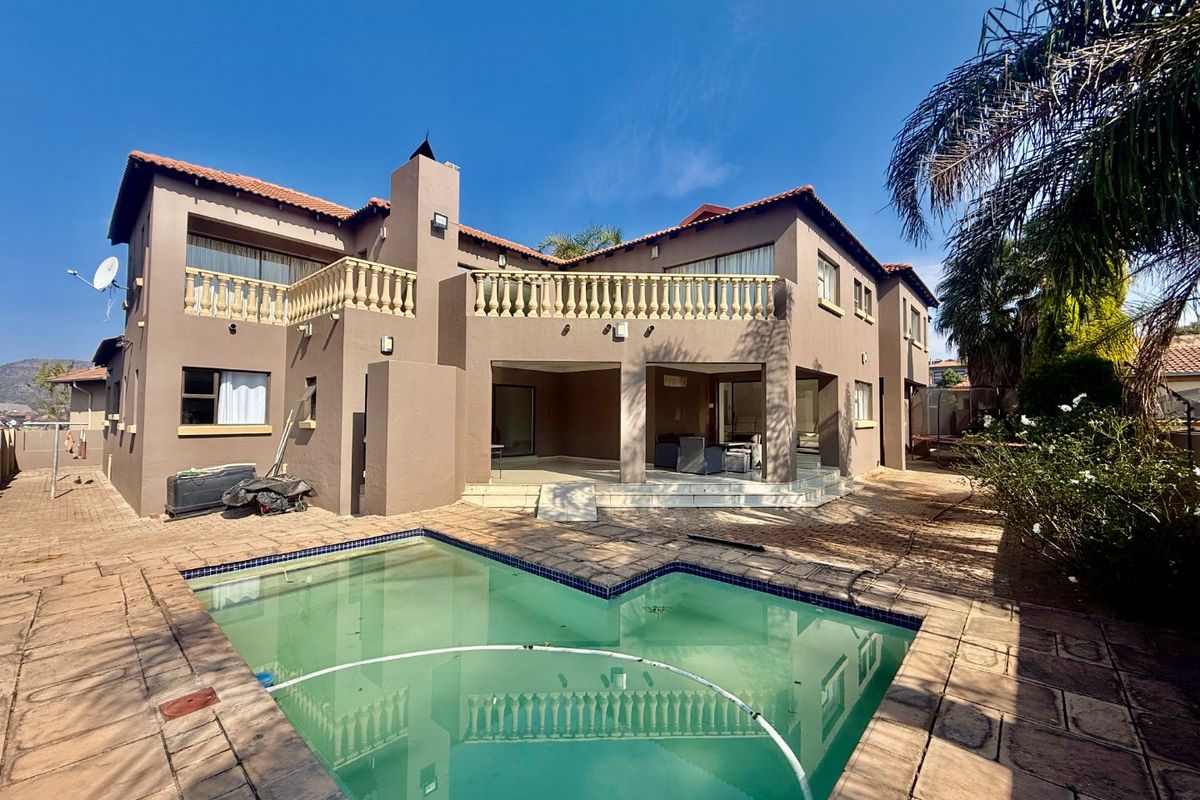 Rear view of the property featuring a swimming pool, covered patio area, and an upper-level balcony with traditional balustrades.