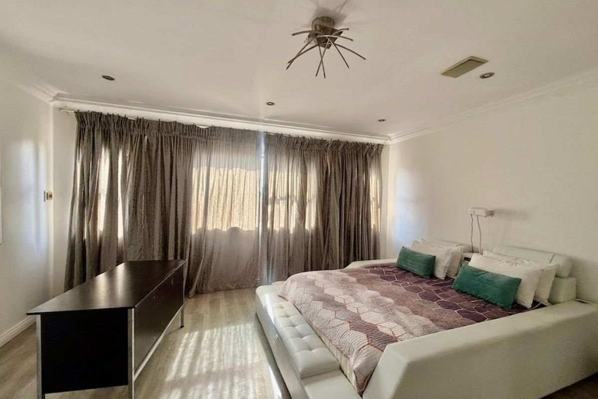 Spacious bedroom featuring laminate flooring, recessed lighting, and large floor-to-ceiling curtains providing ample natural light.