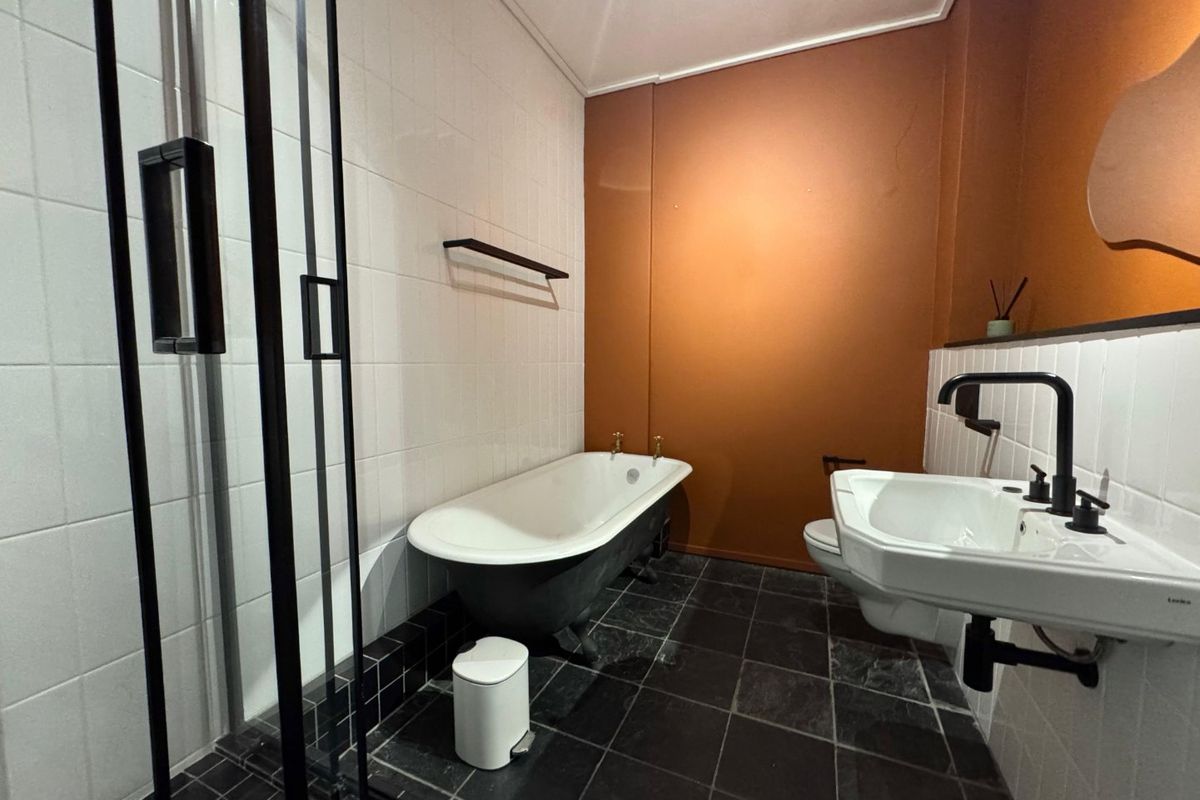 Modern bathroom featuring a freestanding bathtub, walk-in shower with black frame, wall-mounted basin, and contrasting dark floor tiles with a feature wall.