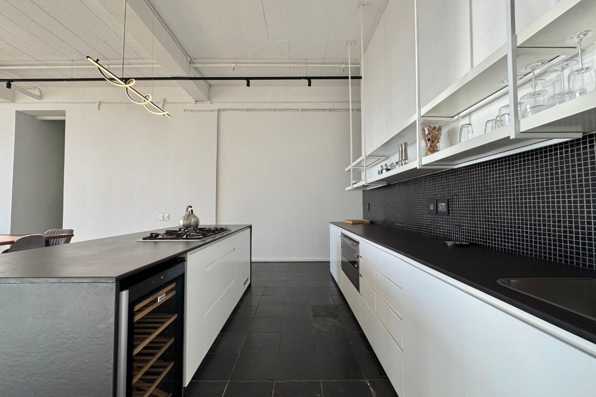Modern kitchen featuring a central island with gas cooktop, integrated wine fridge, sleek white cabinetry, black stone countertops, and a striking mosaic tile backsplash.
