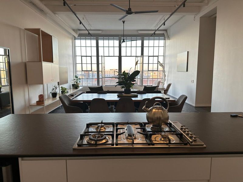 Spacious open-plan living area featuring a modern kitchen island with gas cooktop, industrial-style windows, and high ceilings with exposed ducting.