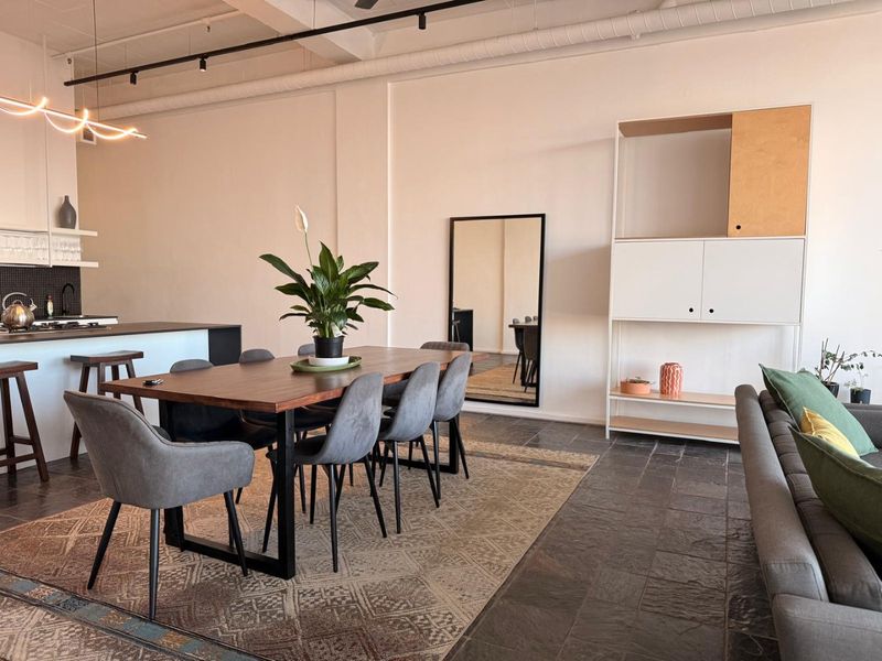 Spacious open-plan living and dining area featuring exposed ceiling beams, track lighting, and durable stone tile flooring, seamlessly connected to a modern kitchen.