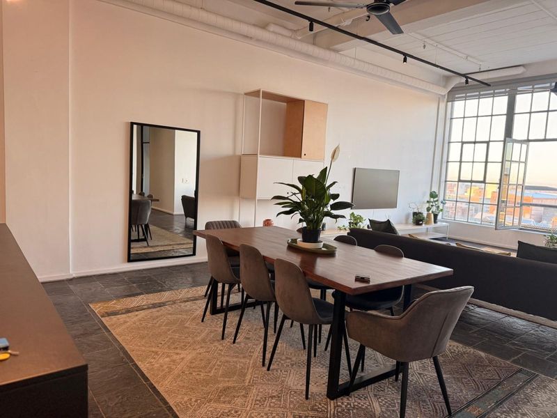 Spacious open-plan living and dining area featuring industrial-style windows, exposed ceiling ducting, and dark slate tile flooring with a modern aesthetic.