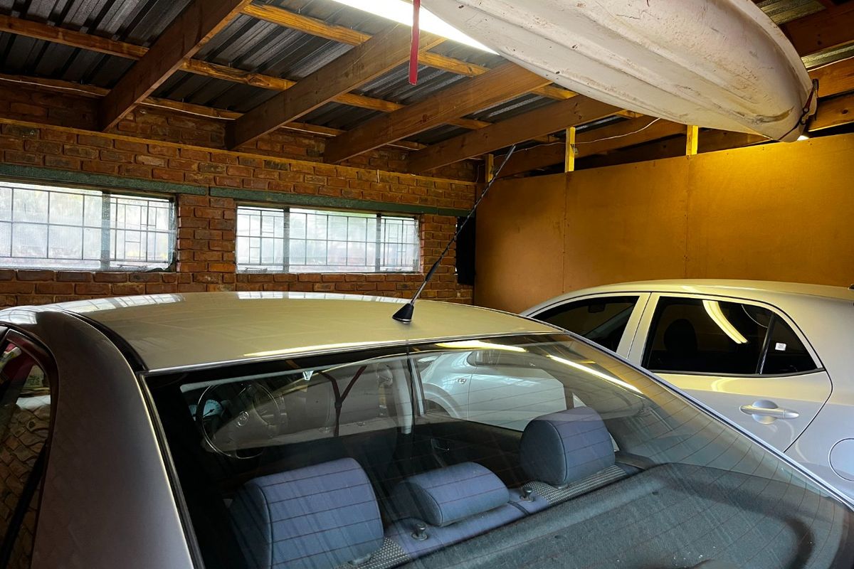 A functional garage space featuring exposed brick walls, timber rafters, and corrugated metal ceiling with integrated fluorescent lighting.