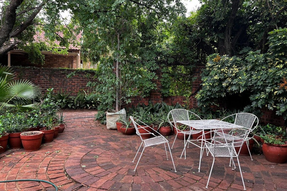 A private garden area featuring circular brick paving and a mature brick boundary wall, surrounded by established trees and greenery.