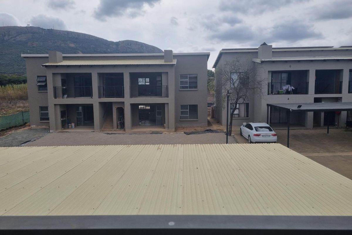Elevated view of apartment complex rear facades featuring balconies, paved parking areas, and corrugated roofing under a cloudy sky.