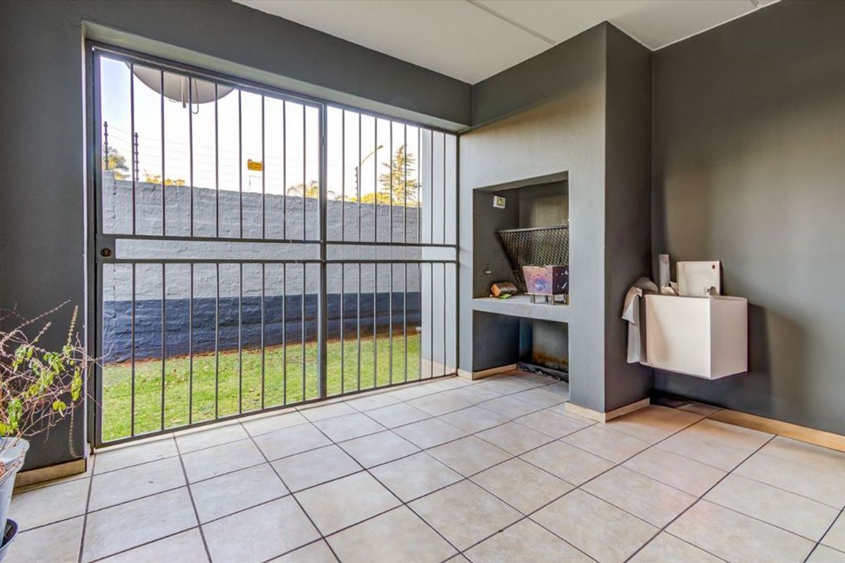 Covered patio area featuring a built-in braai, tiled flooring, and a secure metal gate leading to the rear garden.