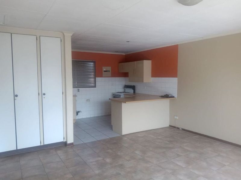 Open plan living area featuring a compact kitchen with built-in cabinetry, breakfast counter, and tiled flooring throughout.