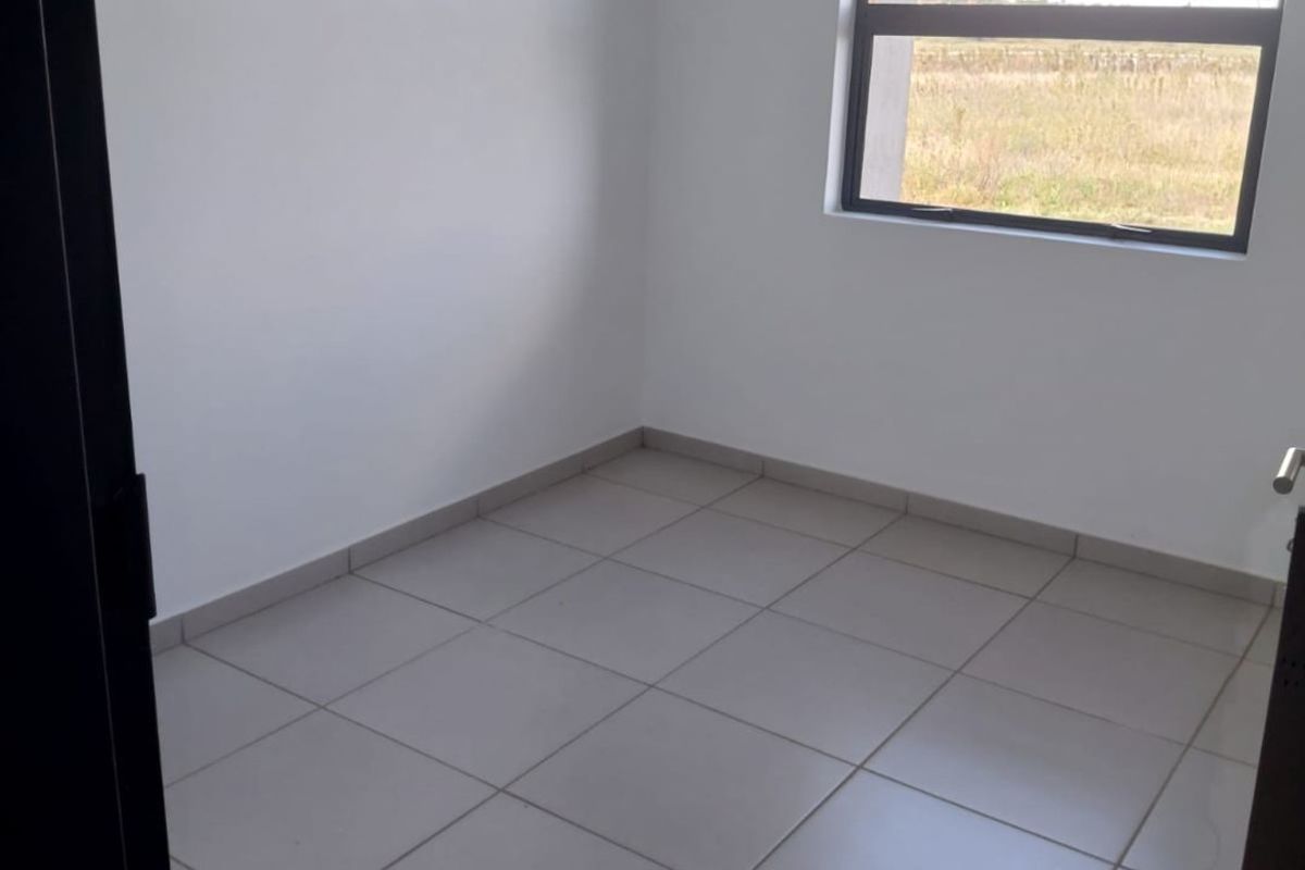 A clean, empty bedroom featuring neutral floor tiles and a large window providing natural light and an exterior view.