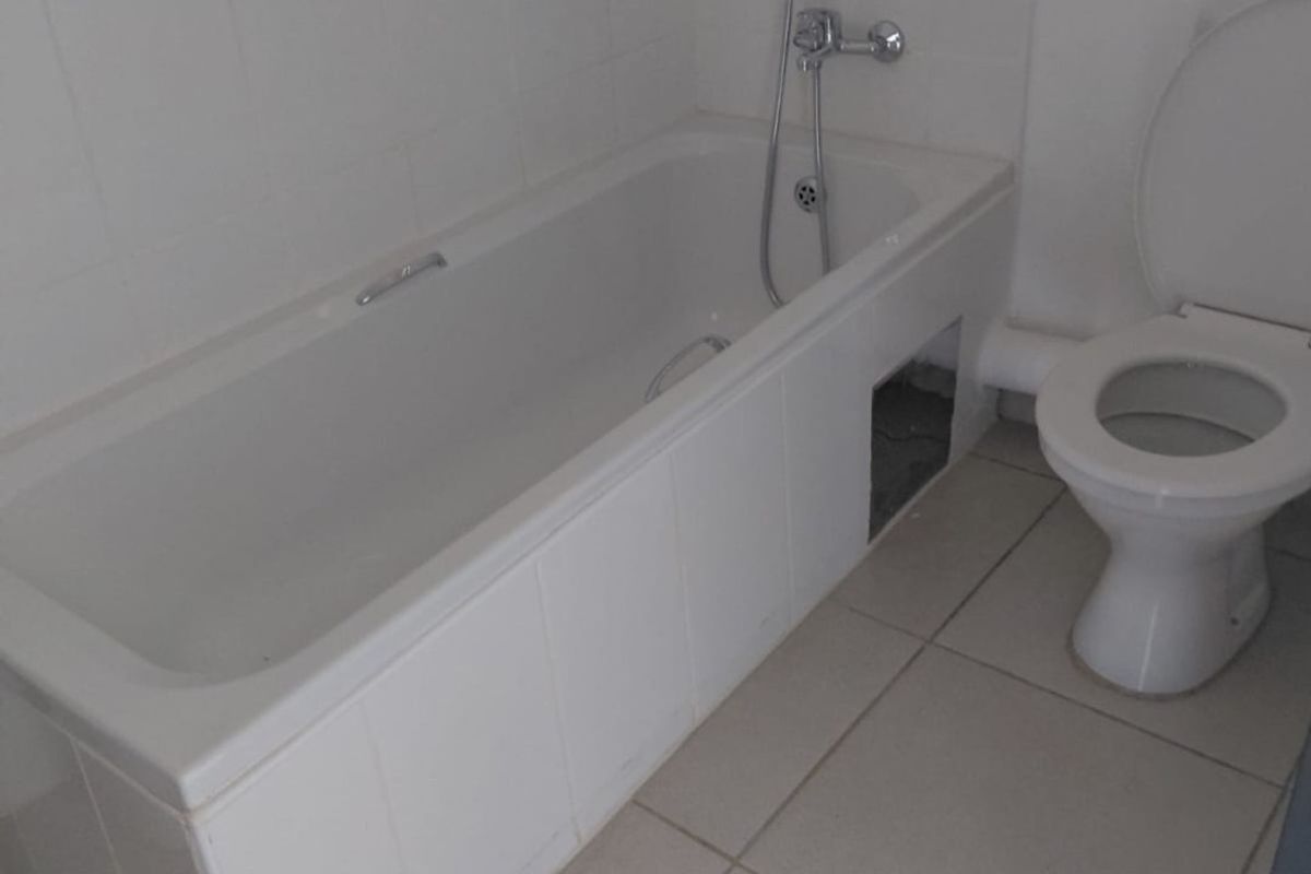 A functional bathroom featuring a standard bathtub with handheld shower attachment and a white ceramic toilet, finished with neutral floor tiling.
