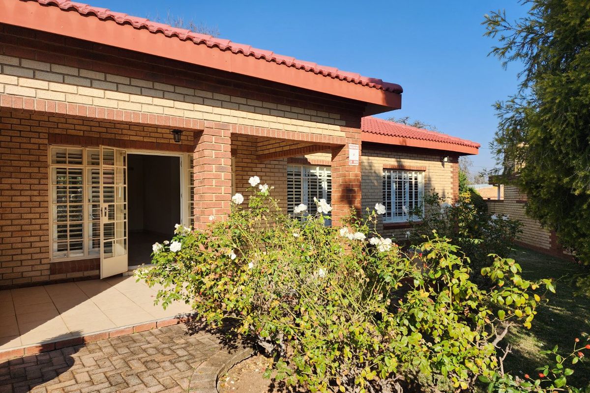 A well-maintained townhouse exterior featuring a face brick facade, tiled roof, and a covered patio area with security shutters overlooking a garden.