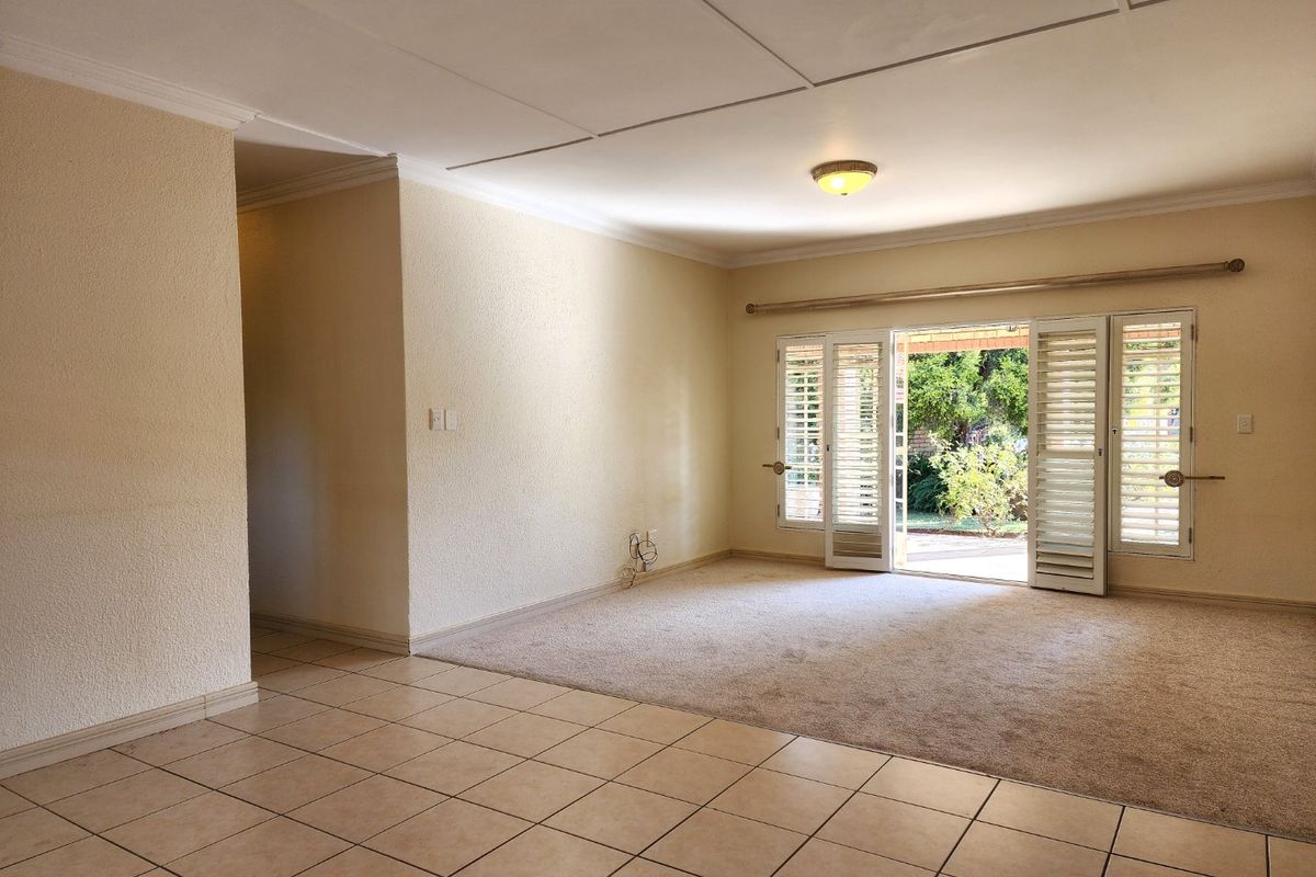 Spacious, empty living area featuring a combination of tiled and carpeted flooring, with direct access to the garden through louvered glass doors.