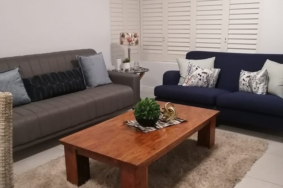 A well-maintained living room featuring neutral tiled flooring, white walls, and white plantation shutters, providing a bright and clean living space.