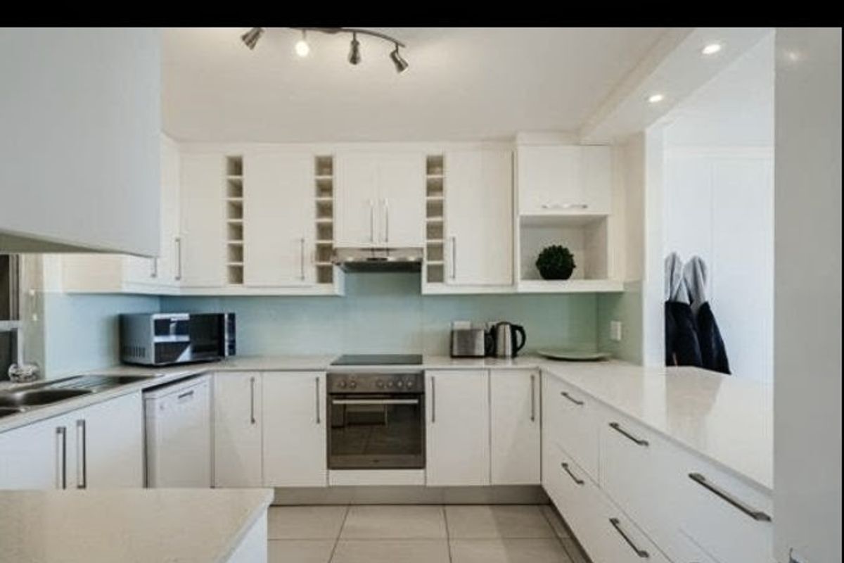 Modern kitchen featuring white cabinetry, stone countertops, integrated appliances, and tiled flooring, offering a clean and functional workspace.