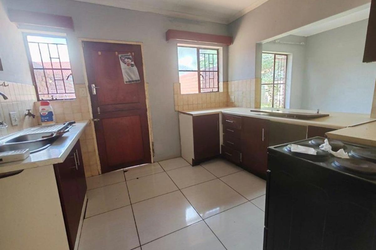 Functional kitchen featuring built-in cabinetry, laminate countertops, stainless steel sink, and tiled flooring, offering a practical layout with potential for modern updates.
