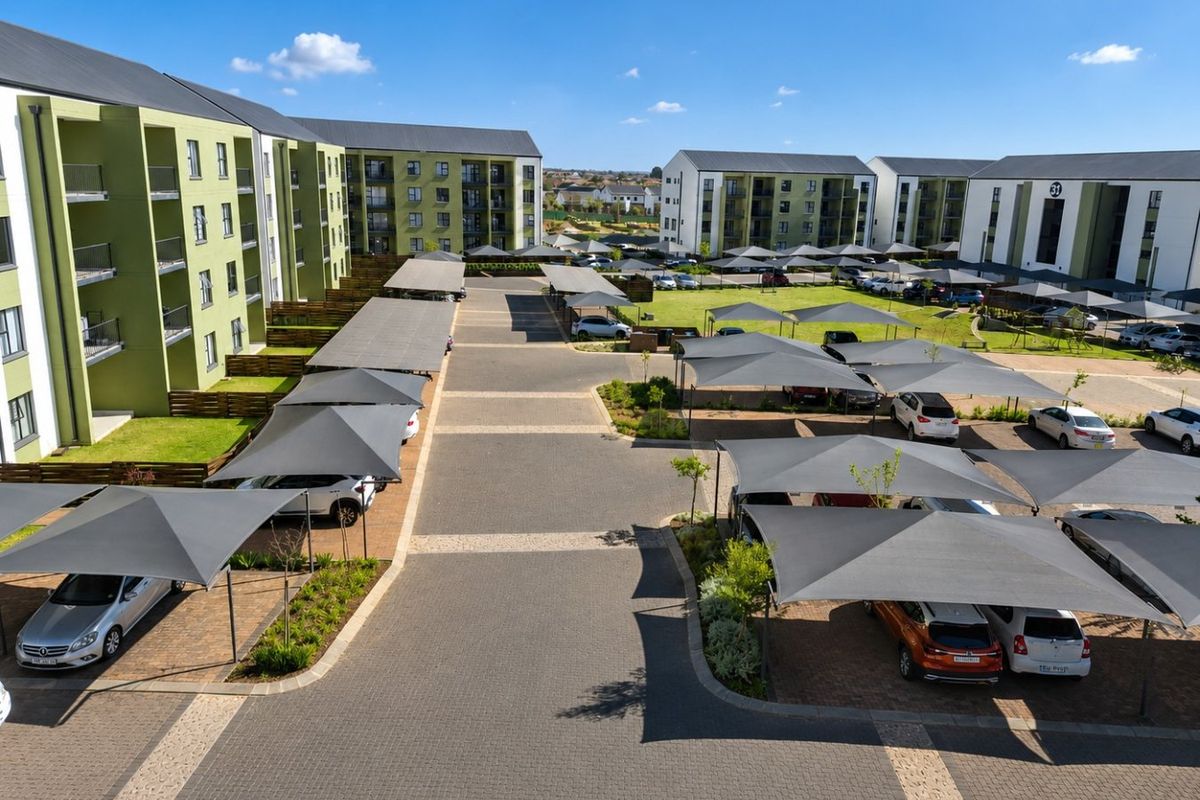 Aerial view of a modern apartment complex featuring paved driveways, extensive shade cloth carports, and well-maintained landscaped garden areas.