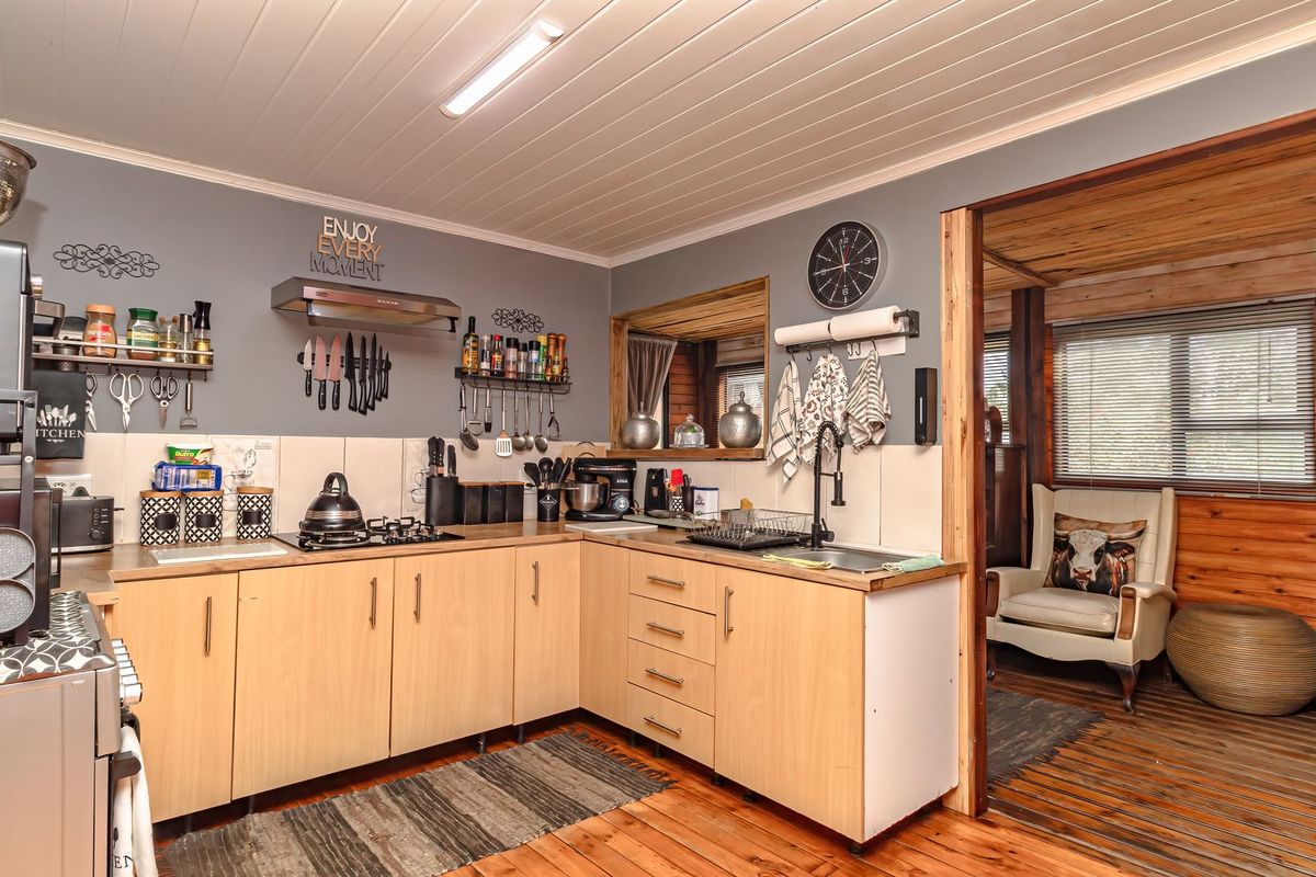 A functional kitchen featuring light wood cabinetry, a gas hob with extractor fan, tiled splashbacks, and direct access to an adjacent living area.
