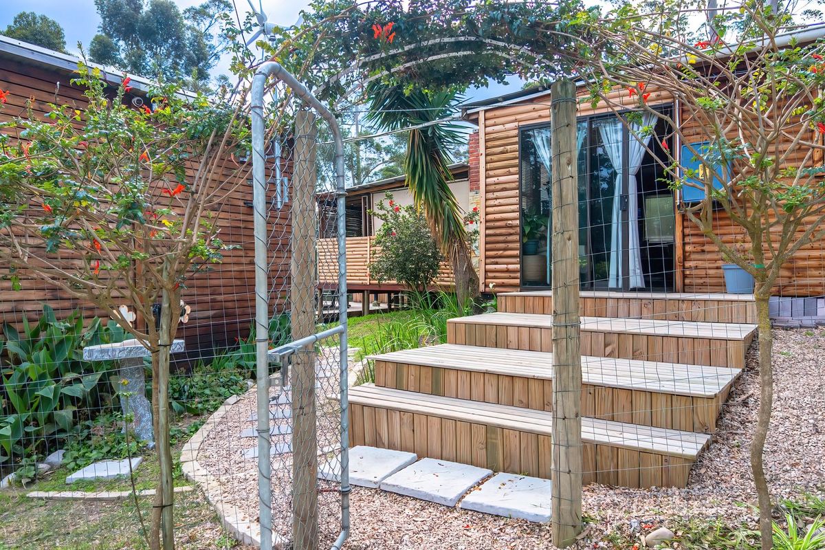 Rear exterior view of a timber log cabin featuring a set of wooden deck steps leading to a sliding glass door entrance.
