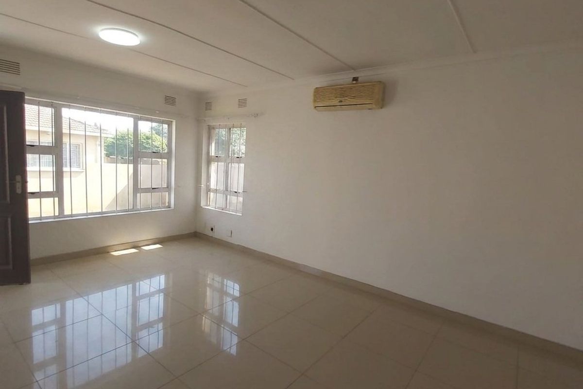 A bright, empty living room featuring polished tile flooring, large windows with security bars, and a wall-mounted air conditioning unit.