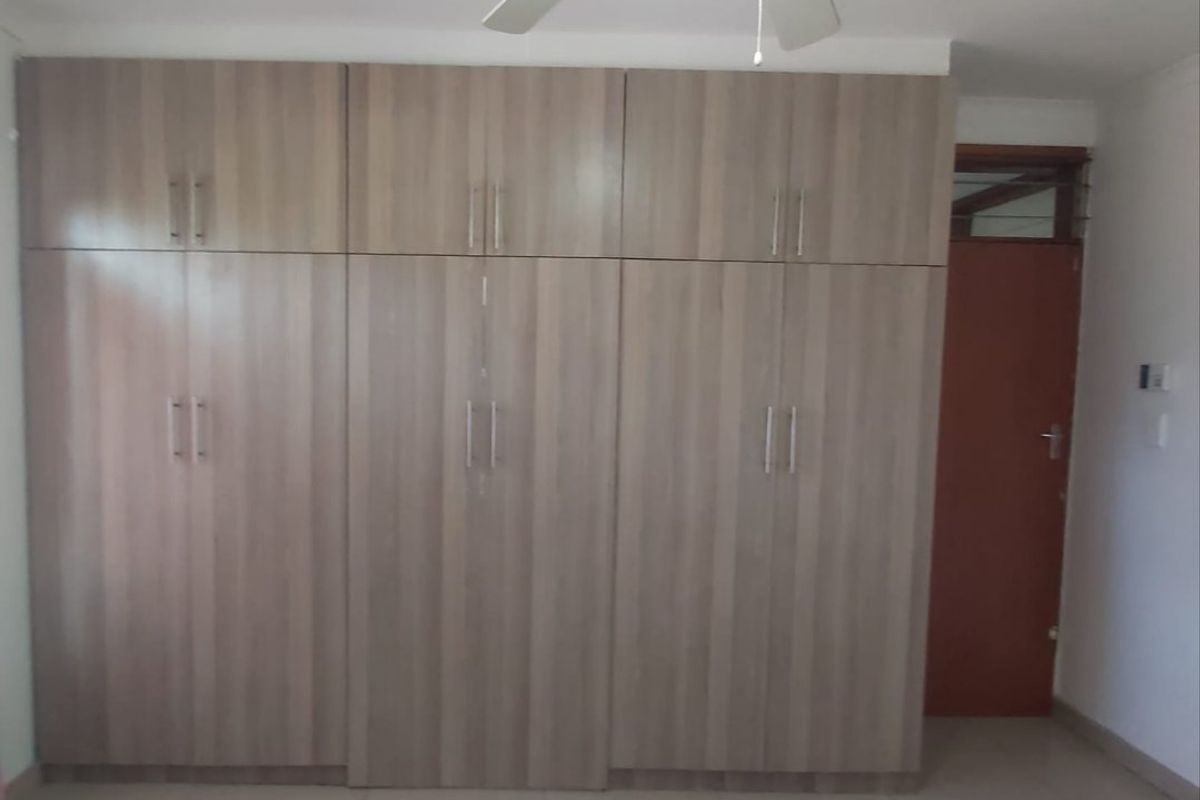 A bedroom featuring extensive built-in wooden cupboards, a ceiling fan, and neutral tiled flooring.
