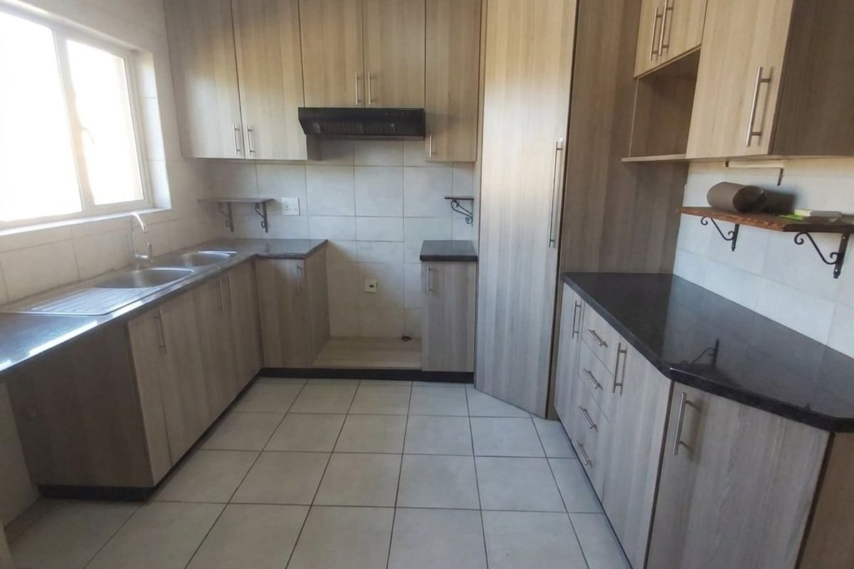 A clean and functional kitchen featuring light wood-tone cabinetry, dark granite countertops, tiled flooring, and a built-in extractor fan.
