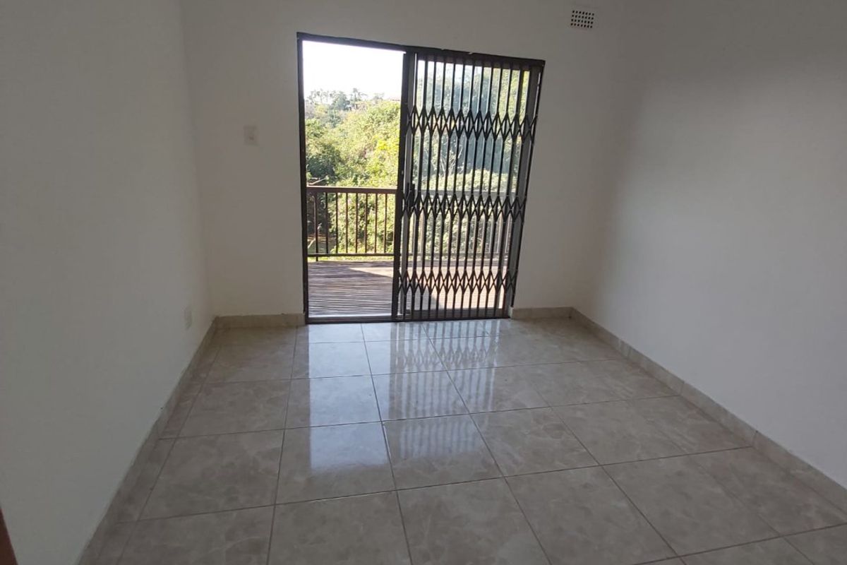 An empty bedroom featuring tiled flooring and a sliding glass door with a security gate leading out to a balcony.