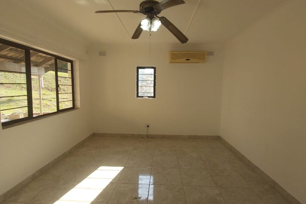 An empty, well-lit living room featuring tiled flooring, a ceiling fan, and a wall-mounted air conditioning unit.