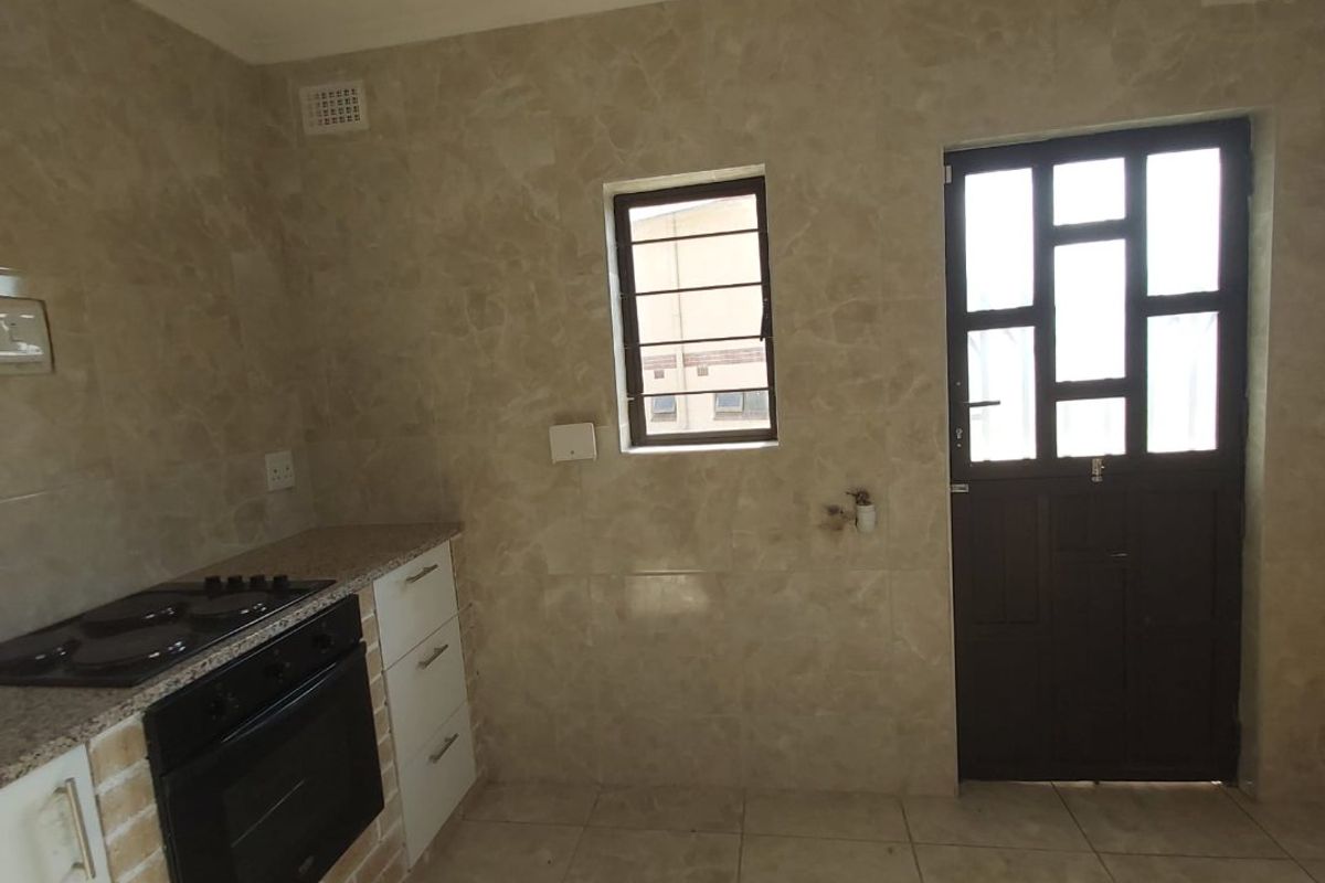 A functional kitchen featuring tiled walls and flooring, built-in oven and hob, granite countertops, and direct access to the exterior via a security door.