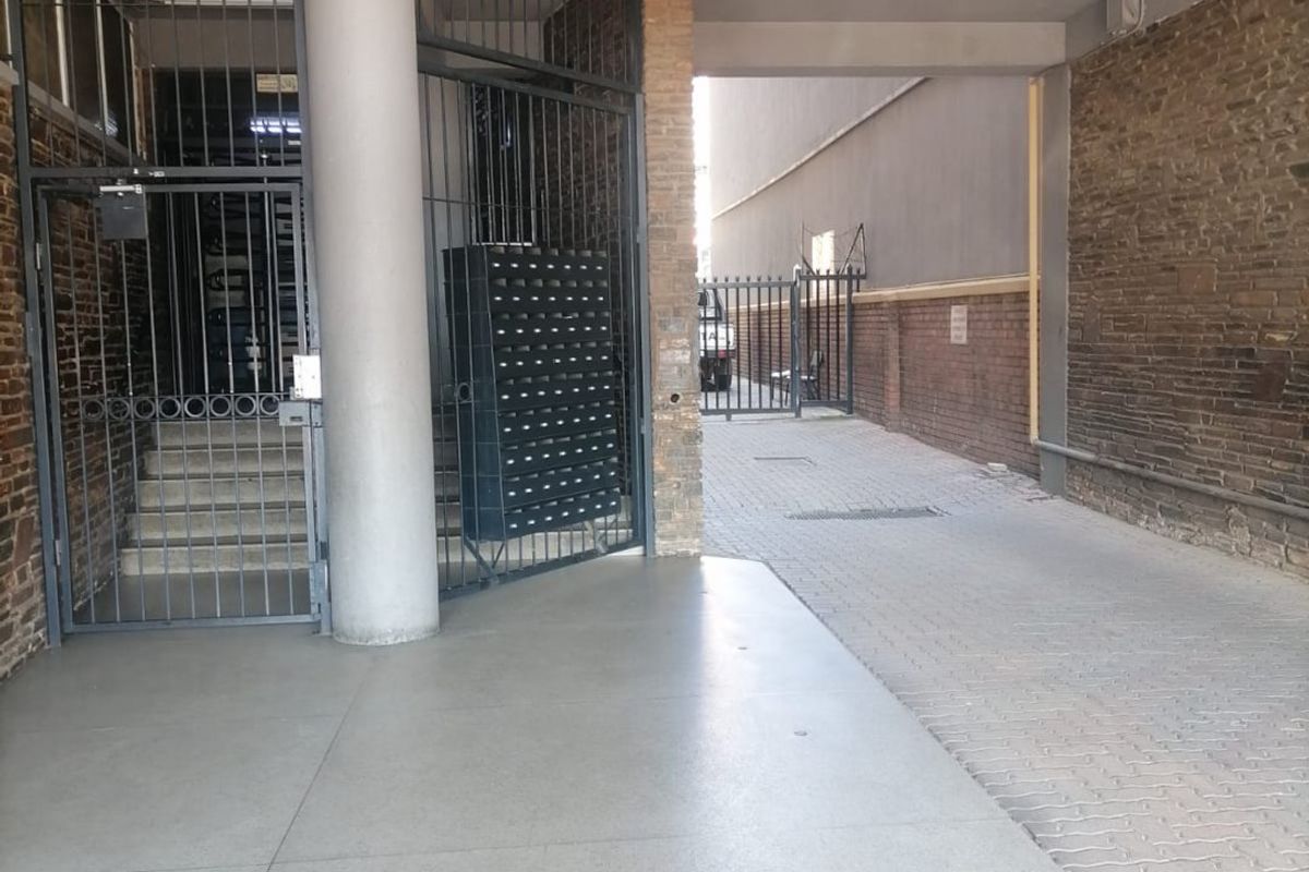 A secure building entrance featuring a concrete walkway, brick wall detailing, and a metal security gate with integrated post boxes.