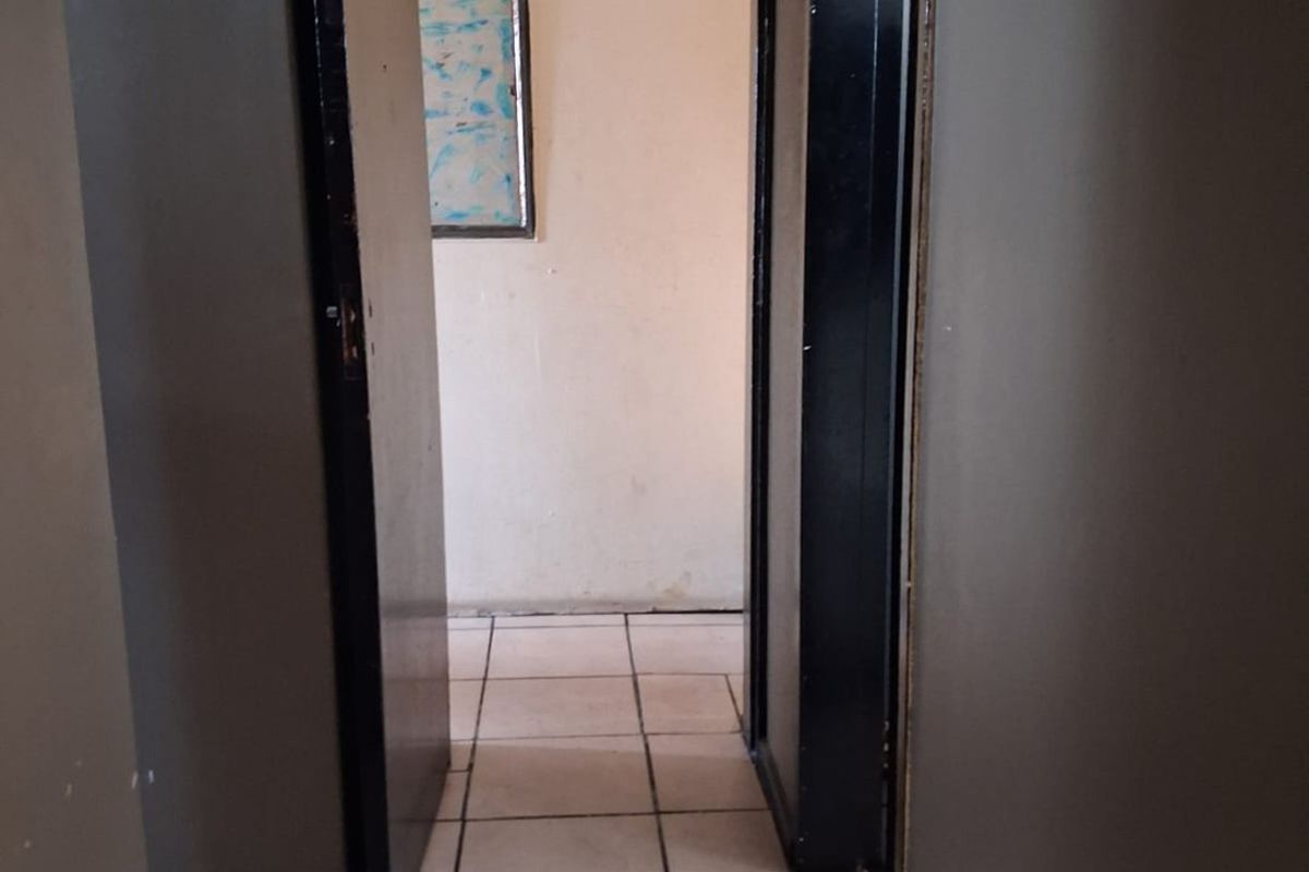 A narrow interior hallway featuring ceramic floor tiles and dark door frames, showing signs of wear and requiring cosmetic updates.