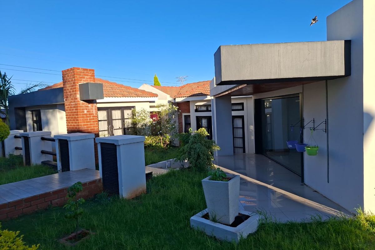 Rear view of the property featuring a tiled patio, brick chimney detail, and sliding glass doors leading into the home, set within a garden area.