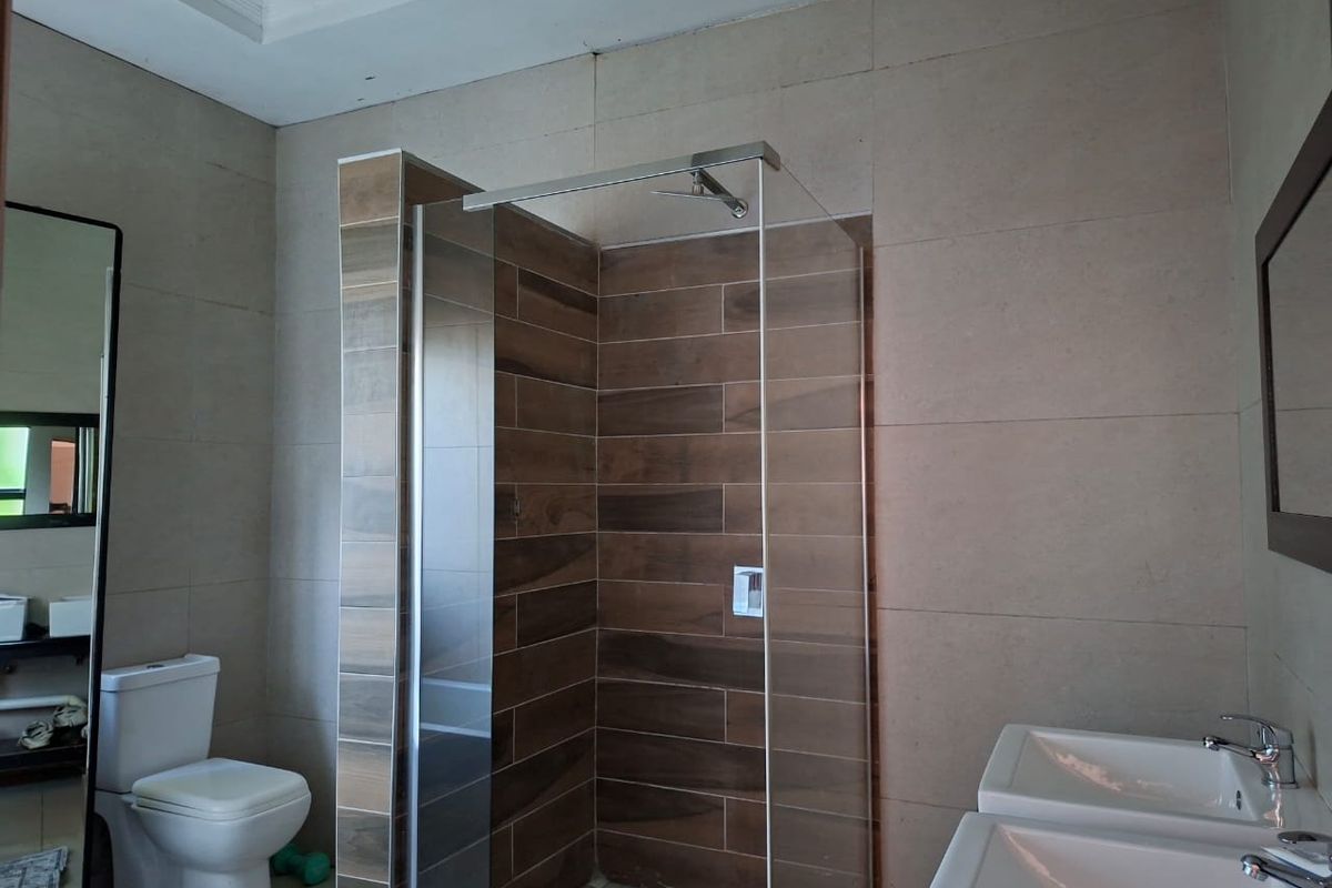 Modern bathroom featuring a walk-in shower with wood-look tiling, dual vanity basins, and neutral wall tiles.