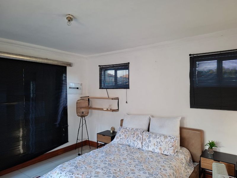 A bedroom featuring tiled flooring, venetian blinds, and an exposed electrical distribution board on the wall.