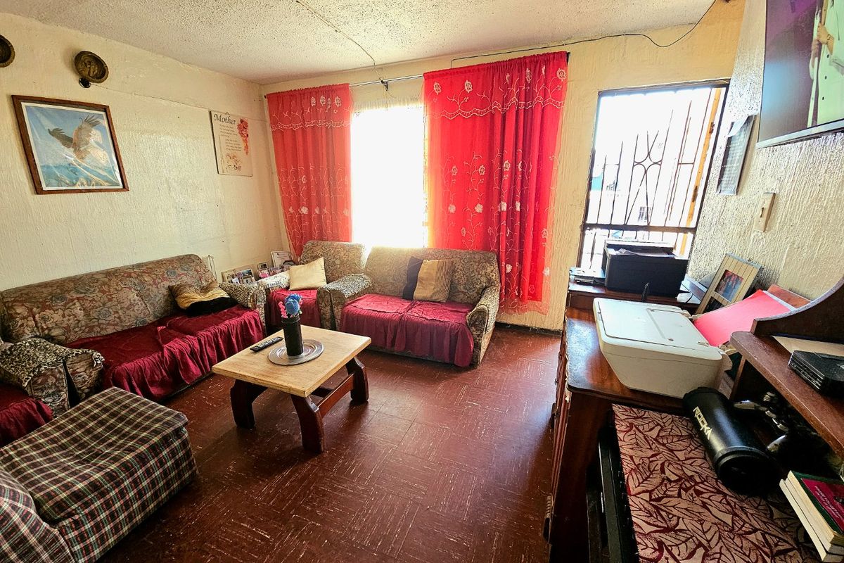 A living room featuring textured ceilings, vinyl flooring, and a security gate, offering a functional space with potential for cosmetic updates.