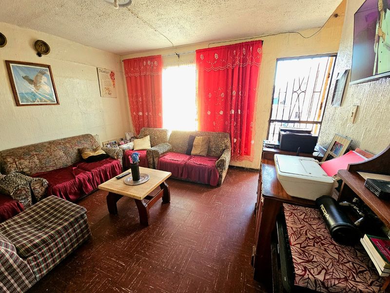 A living room featuring textured ceilings, vinyl flooring, and a security gate, offering a functional space with potential for cosmetic updates.