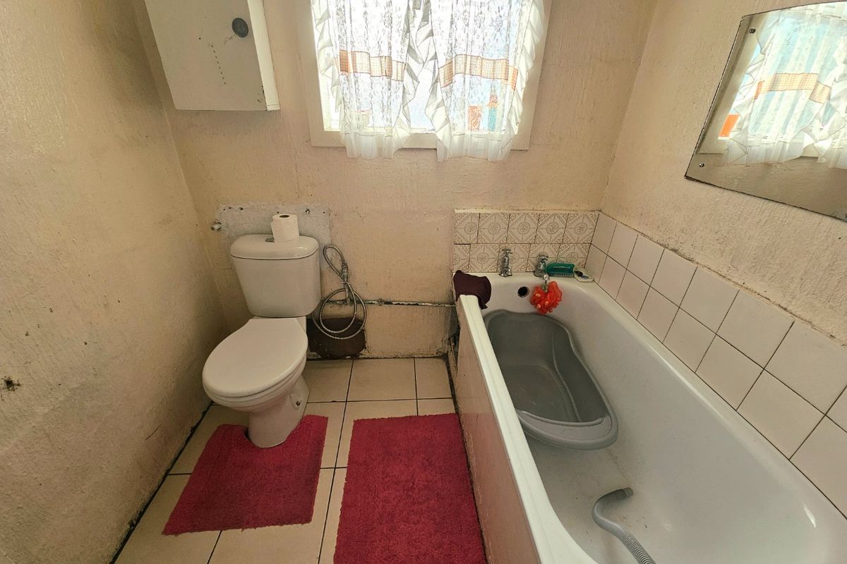 A dated bathroom featuring a standard toilet and bathtub with tiled splashbacks, requiring cosmetic updates and wall repairs.