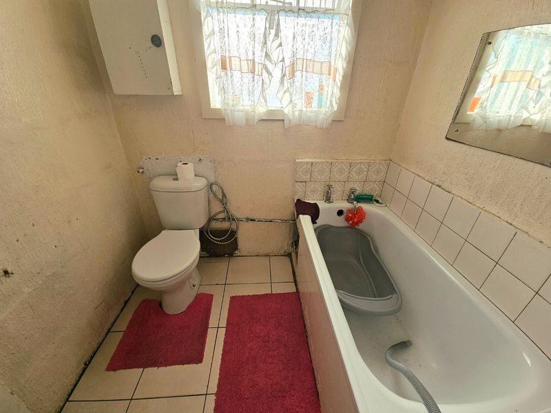 A dated bathroom featuring a standard toilet and bathtub with tiled splashbacks, requiring cosmetic updates and wall repairs.