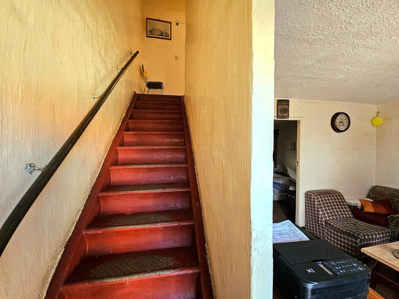 Interior hallway featuring a staircase with a handrail, showing signs of wear and dated finishes throughout the space.