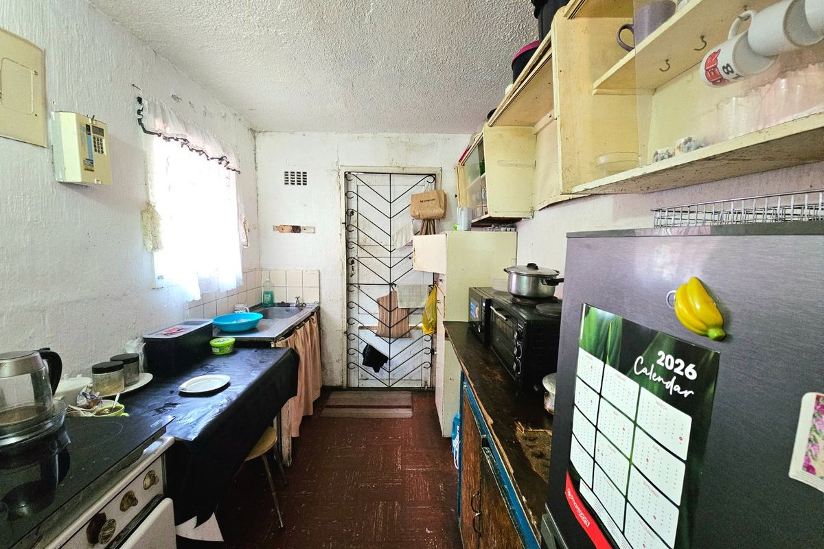 A compact kitchen featuring built-in cabinetry, a stainless steel sink, and a security gate, requiring modernization and cosmetic updates to improve functionality and aesthetic appeal.