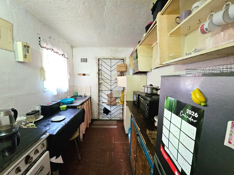 A compact kitchen featuring built-in cabinetry, a stainless steel sink, and a security gate, requiring modernization and cosmetic updates to improve functionality and aesthetic appeal.