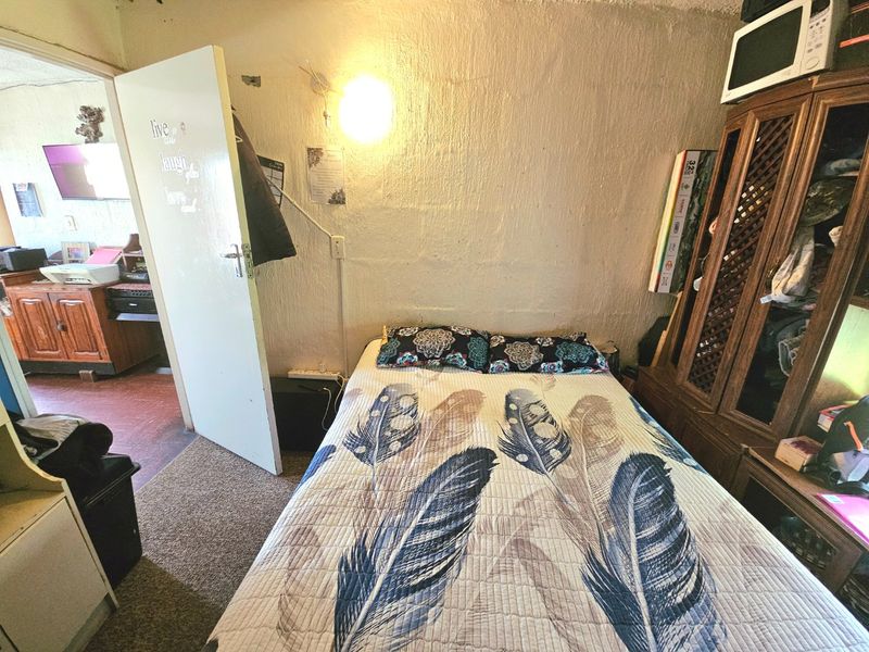 A bedroom featuring textured walls, carpet flooring, and a wall-mounted light fixture, offering a functional space with potential for cosmetic updates.