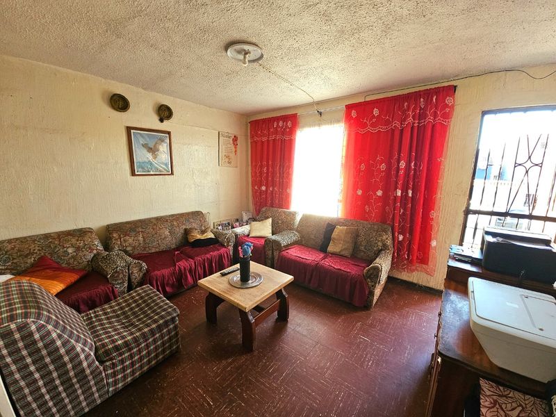 A living room featuring textured ceilings, vinyl floor tiles, and a security gate on the window, offering a dated interior space ready for renovation.
