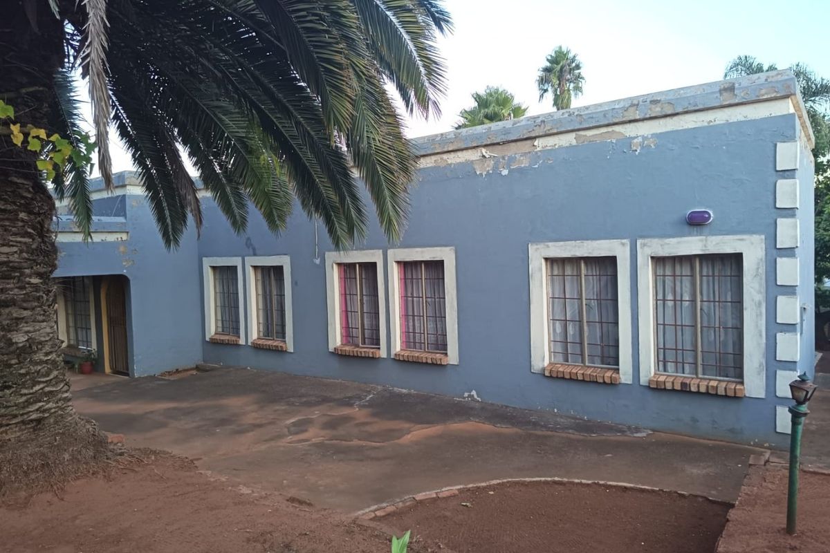 Rear exterior view of the house featuring blue painted walls with security bars on windows and a paved patio area.