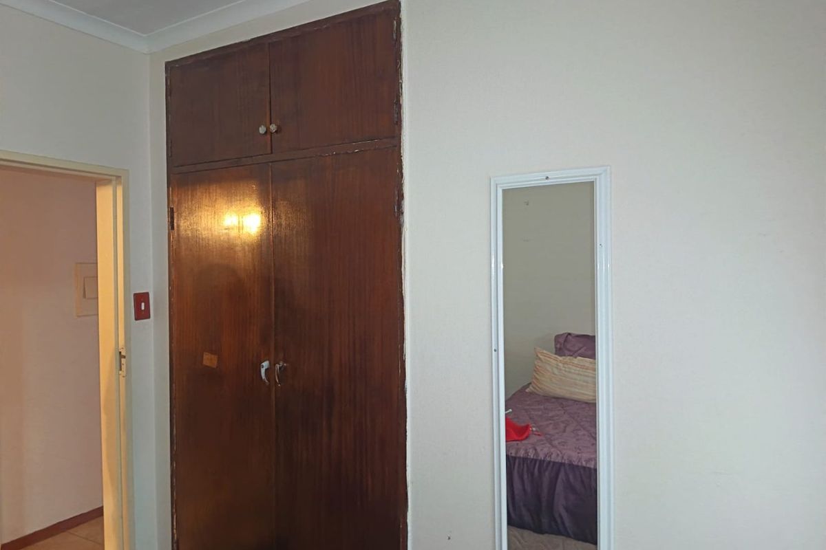 A bedroom featuring a built-in wooden wardrobe with overhead storage and a wall-mounted mirror.