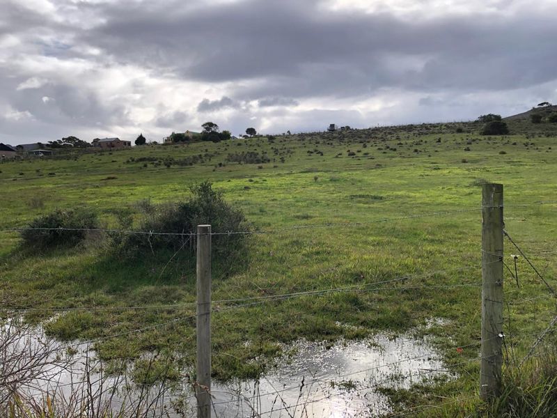 Expansive view of open farm land with a wire fence in the foreground under a cloudy sky.