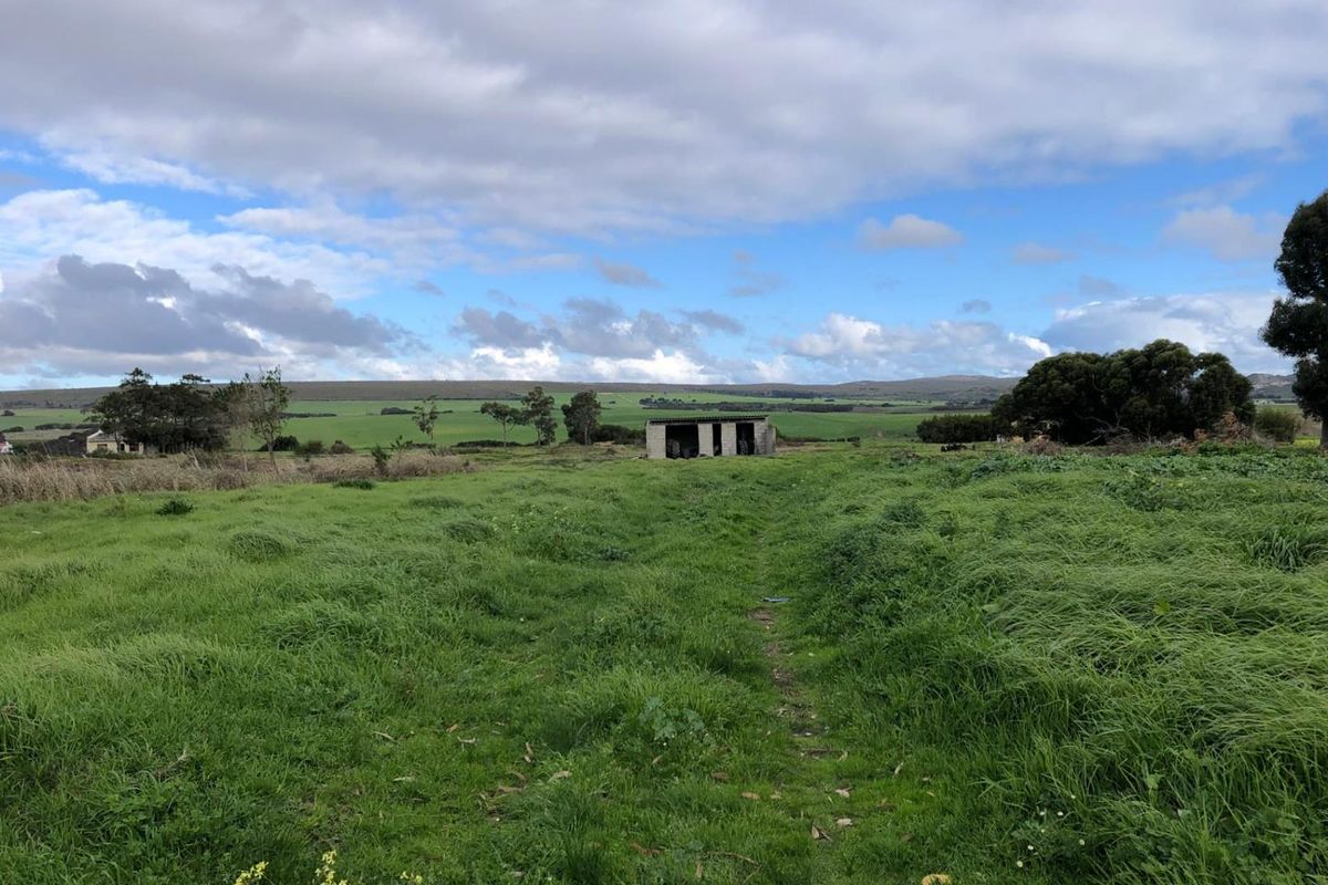 A wide view of a rural farm property featuring open pasture land and a small, weathered outbuilding in the distance.