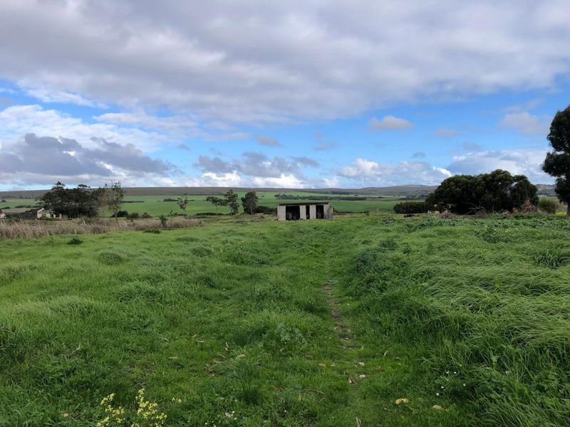 A wide view of a rural farm property featuring open pasture land and a small, weathered outbuilding in the distance.