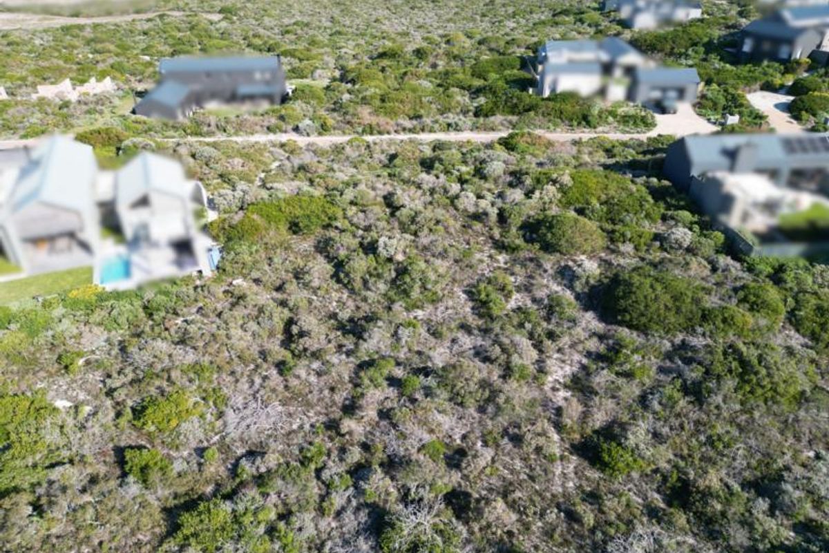 An aerial view of a vacant residential plot covered in natural coastal vegetation, situated within a developed residential estate.