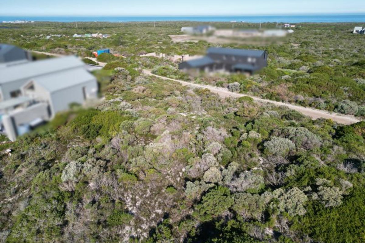 An aerial view of a vacant residential plot featuring natural coastal vegetation with surrounding residential development and distant ocean views.