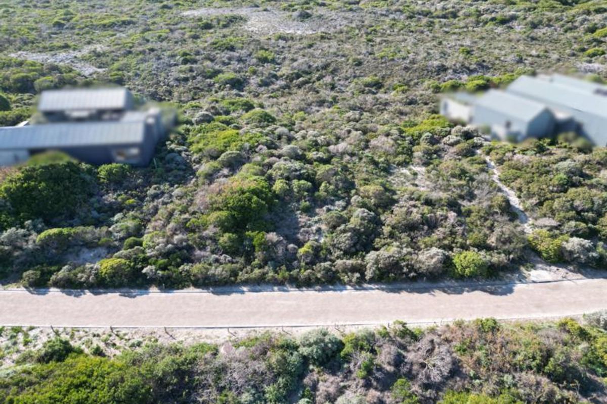 An aerial view of a vacant residential plot featuring natural coastal vegetation and direct access to a paved road.